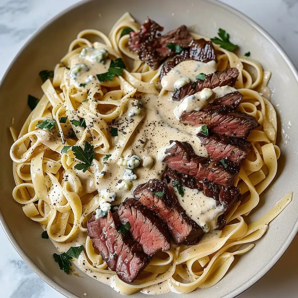 Une assiette de fettuccine recouverte de steak et de sauce crémeuse, parsemée de persil et de fromage bleu.