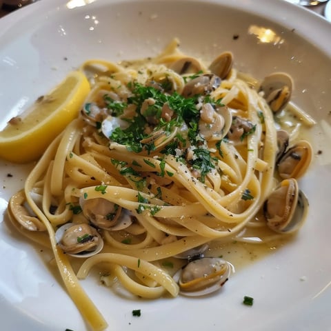 Des linguines garnies de palourdes, persil frais et une rondelle de citron.